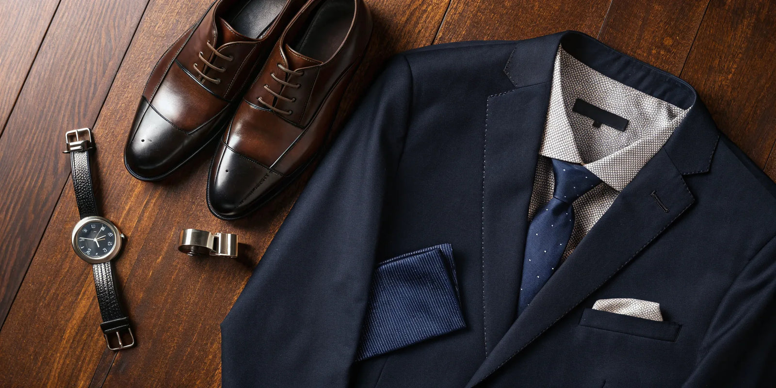 Men's clothing subscription box featuring a stylish navy suit, dress shoes, watch, and tie.